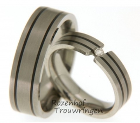 Titanium trouwringen, welke een breedte hebben van 5 mm. De ring is prachtig versierd met twee smalle, zwarte keramische ringen. Als middelpunt is in de dames trouwring een zwevende, briljant geslepen diamant van 0,05 ct gezet.