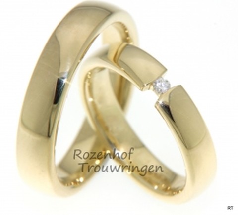 Hoogglanzende, geelgouden trouwringen. De ringen zijn 5 mm breed. In de dames trouwring lijkt een briljant geslepen diamant gevangen te zitten tussen de ring. De diamant is 0,04 ct.