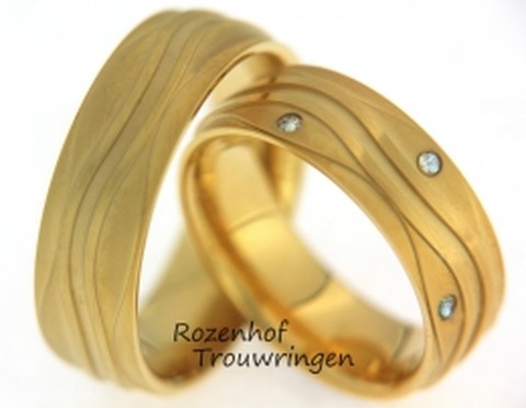 Frivole, geelgouden trouwringen van 7 mm breed. De lijnen geven de ring een frivool karakter. In de dames trouwring zijn verdeeld, 8 briljant geslepen diamanten gezet van in totaal 0,12 ct.
