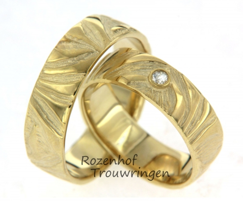 Deze schitterden trouwringen zijn uitgevoerd in geelgoud met een breedte van 6,3 mm. De ringen hebben een mooi organisch motief. In de damesring is één diamant gezet van 0,04 ct. De diamant is briljant geslepen en staat centraal in de ring. Dit mooie setje is leverbaar in 9, 14 en 18 karaat goud.