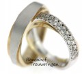 Exclusieve trouwringen van wit- en geelgoud met diamanten. De ringen bestaan uit twee banen die schuin over elkaar gezet zijn. De bovenste baan van de dames trouwring is rijkelijk bezet met briljant geslepen diamanten. Een pronkstuk!